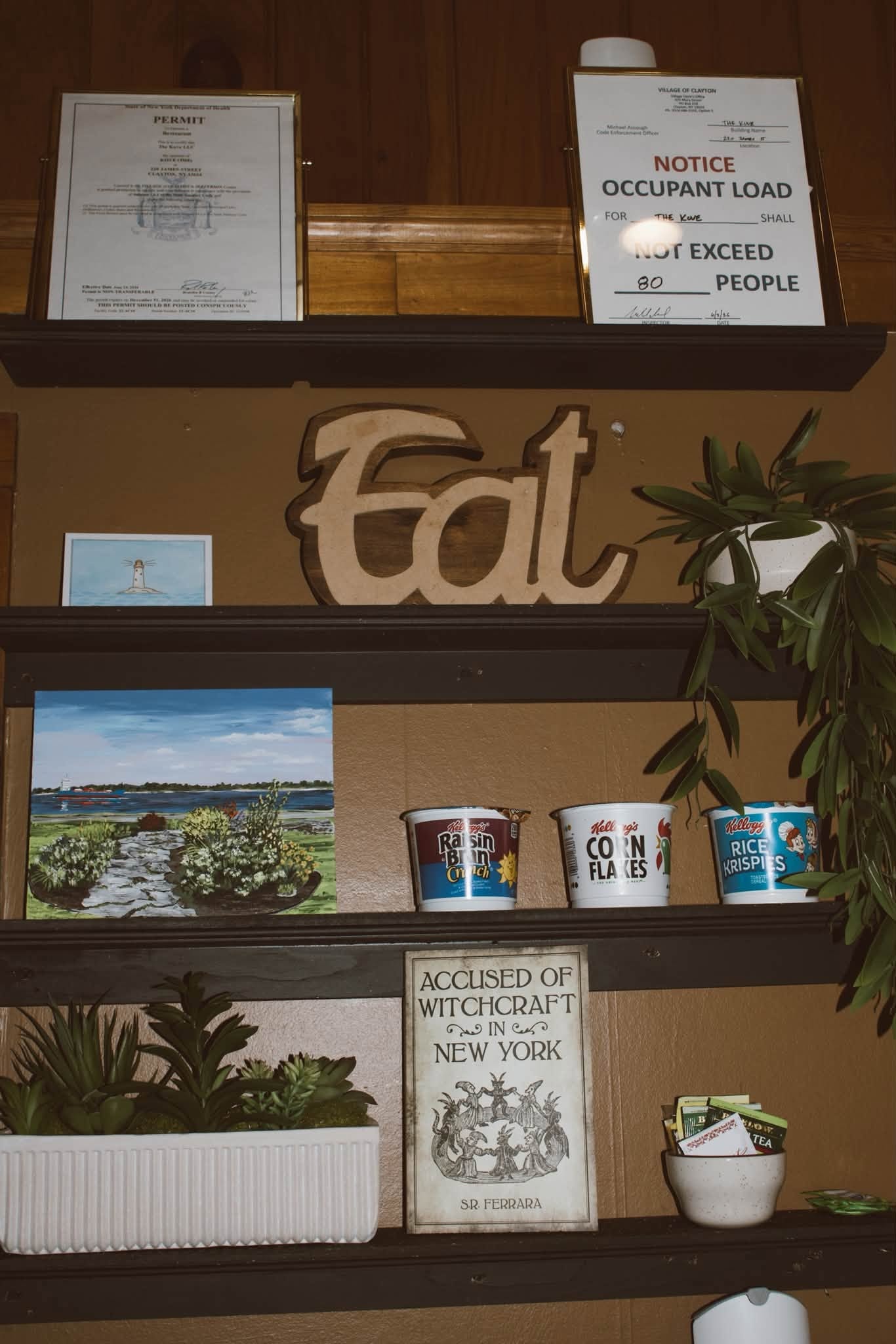 Interior shelves with "Eat" sign, local art, and plants at The Kove